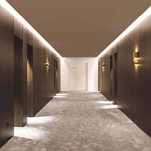 Photo d'ambiance représentant un couloir éclairé, avec un sol clair et des murs foncés.  